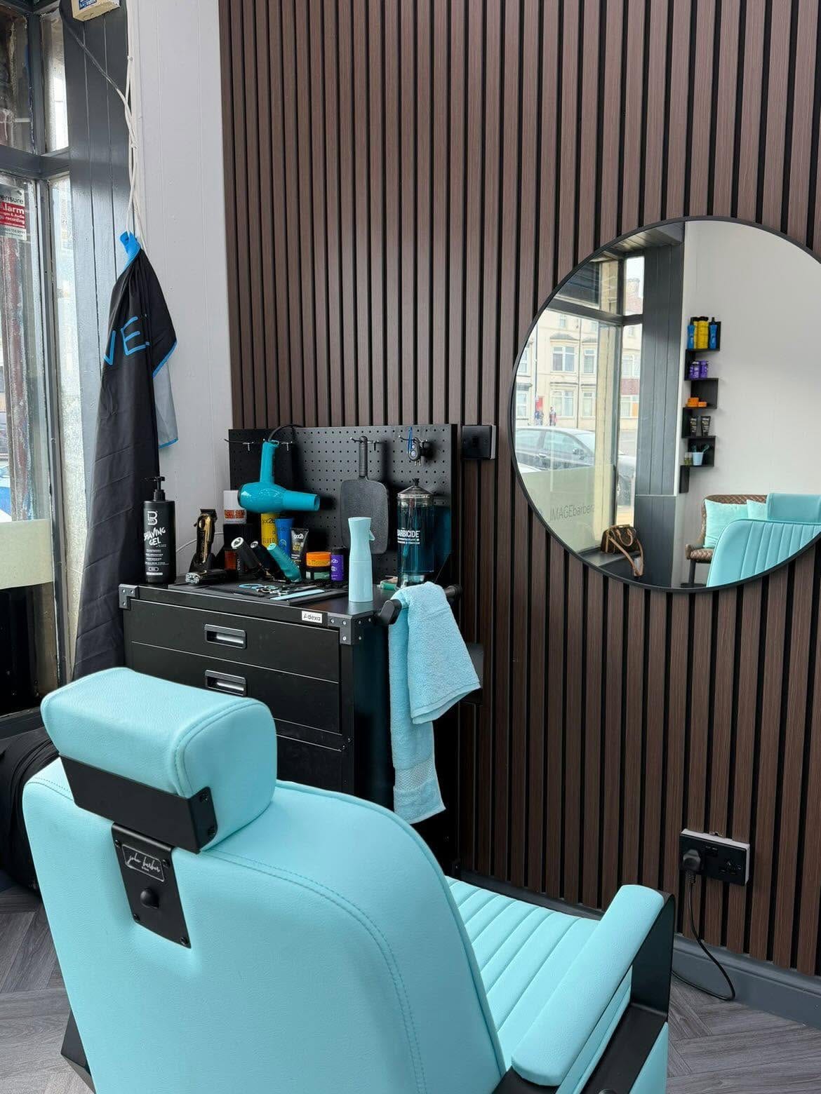 A turquoise barber chair in front of a black station and round mirror at Image Barberz, Redcar