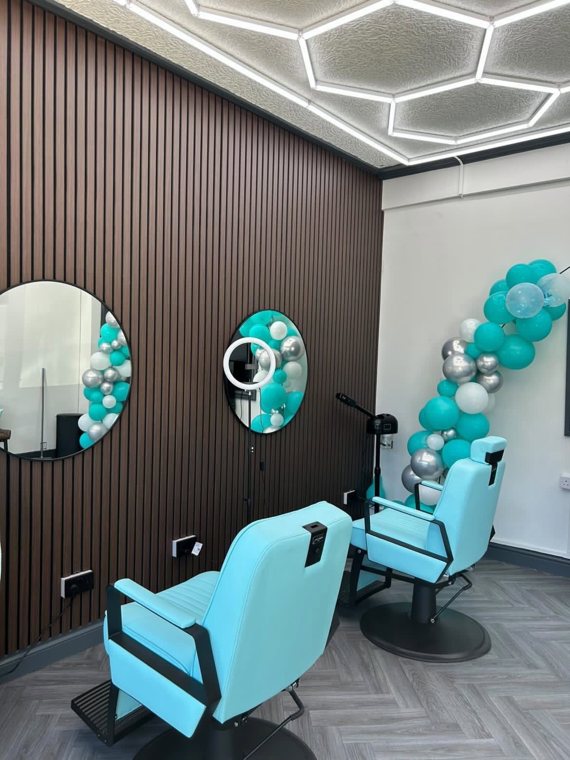 Two turquoise barber chairs against a dark slatted wall inside Image Barberz
